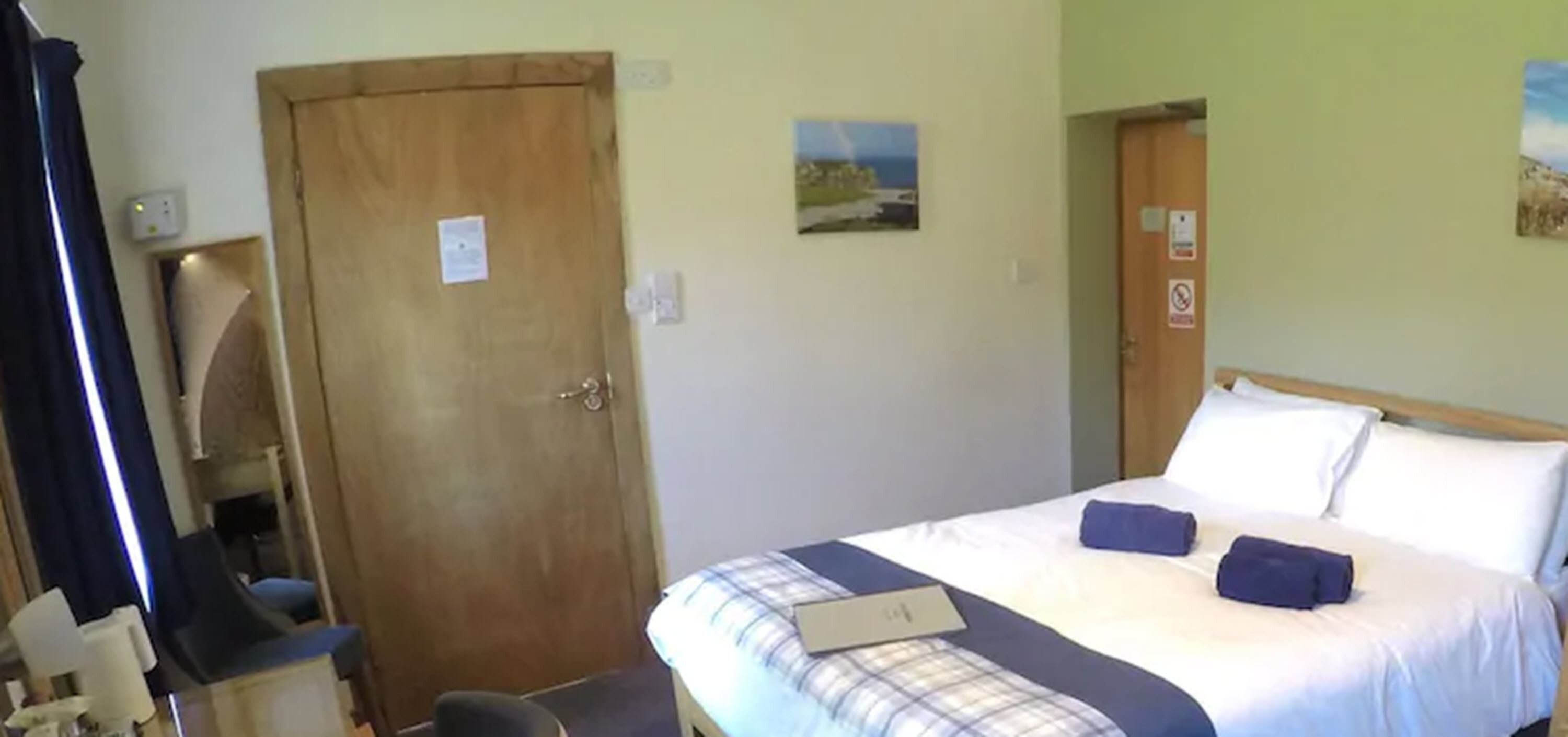 A hotel room with a bed, a desk, and a chair. There is a door and a wall with a picture.