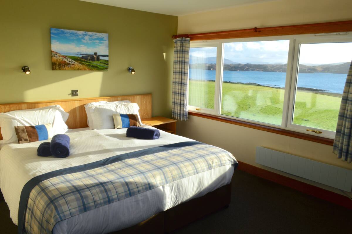 A hotel room with a large bed, a view of the sea, and a painting on the wall.