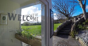 A welcome sign with a view of a green landscape and stone steps leading to a building. - St Columba Hotel (Isle of Iona)