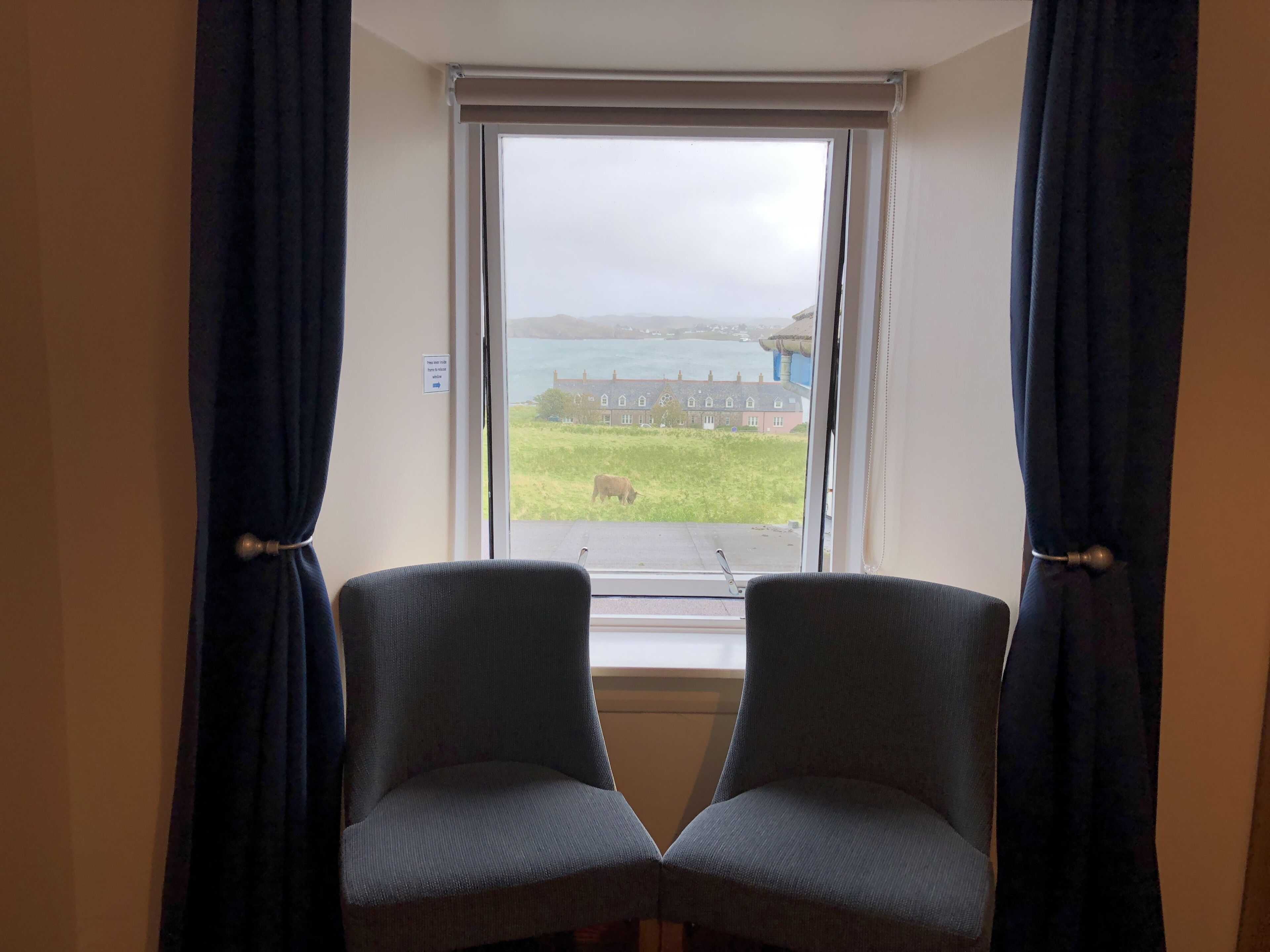 A room with two chairs facing a window overlooking a grassy area and a building.