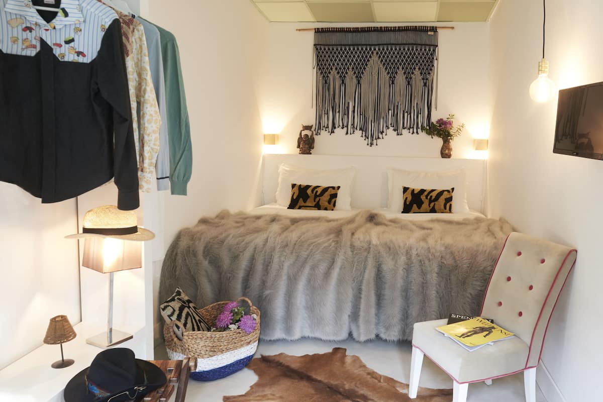 Un dormitorio con una cama, una silla, una lámpara, un adorno de pared y un televisor instalado en la pared.