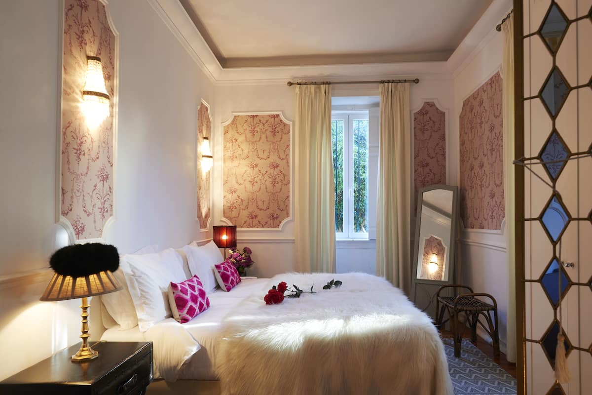 Habitación de hotel con una cama grande, una mesita de noche con lámpara, un aparador y una ventana con cortinas.