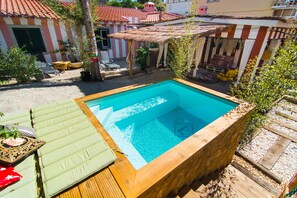 A rectangular swimming pool with a wooden deck and green lounge chairs. - Lucky's Guest House (Cascais)