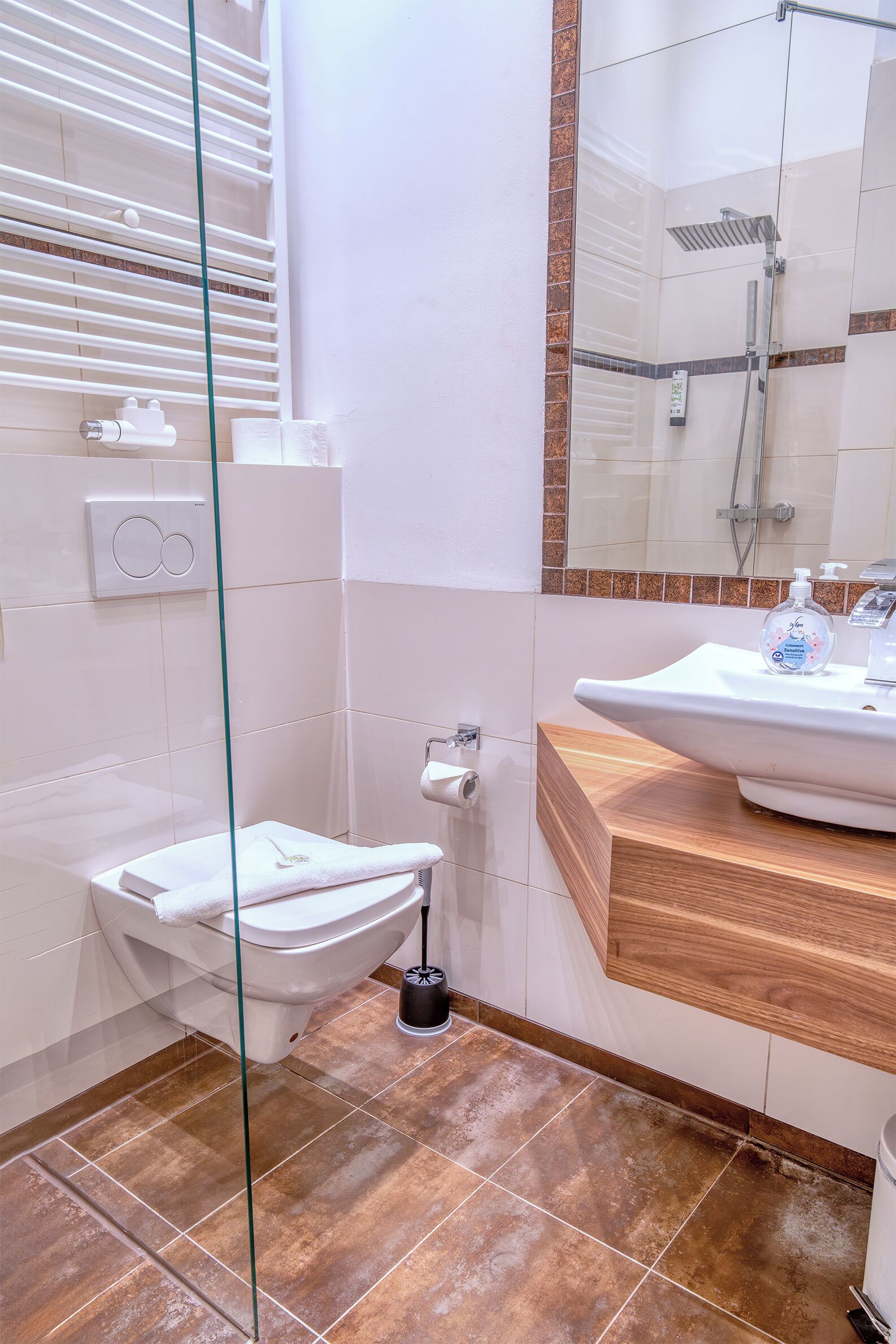 Un baño moderno con cabina de ducha de vidrio, inodoro blanco, lavabo con encimera de madera y espejo sobre el lavabo.