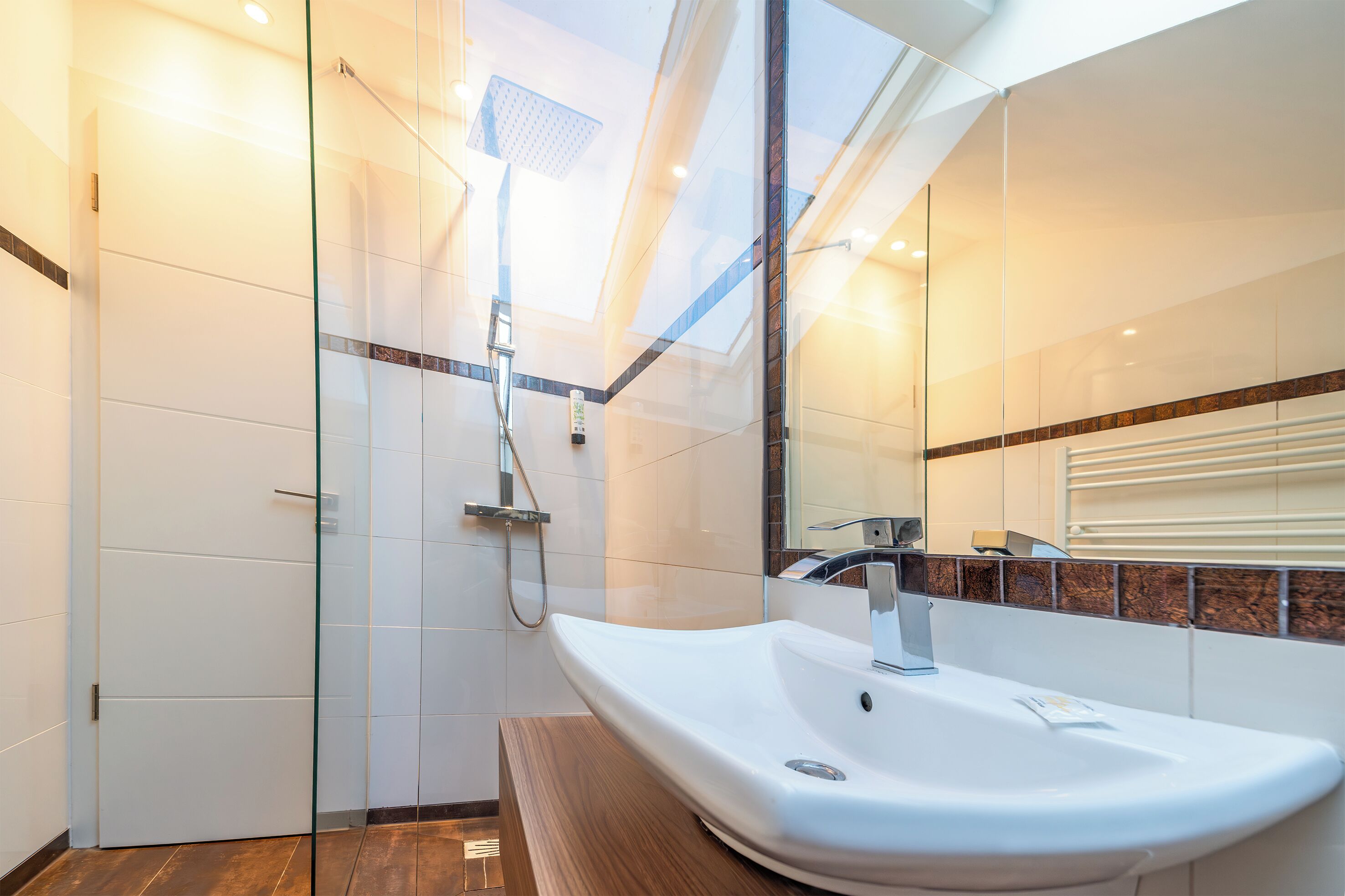 Un bagno moderno con cabina doccia in vetro, lavandino bianco e mobile bagno in legno.