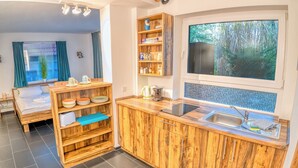 Een compacte keuken met houten kastjes, een spoelbak en een raam met uitzicht op groen.