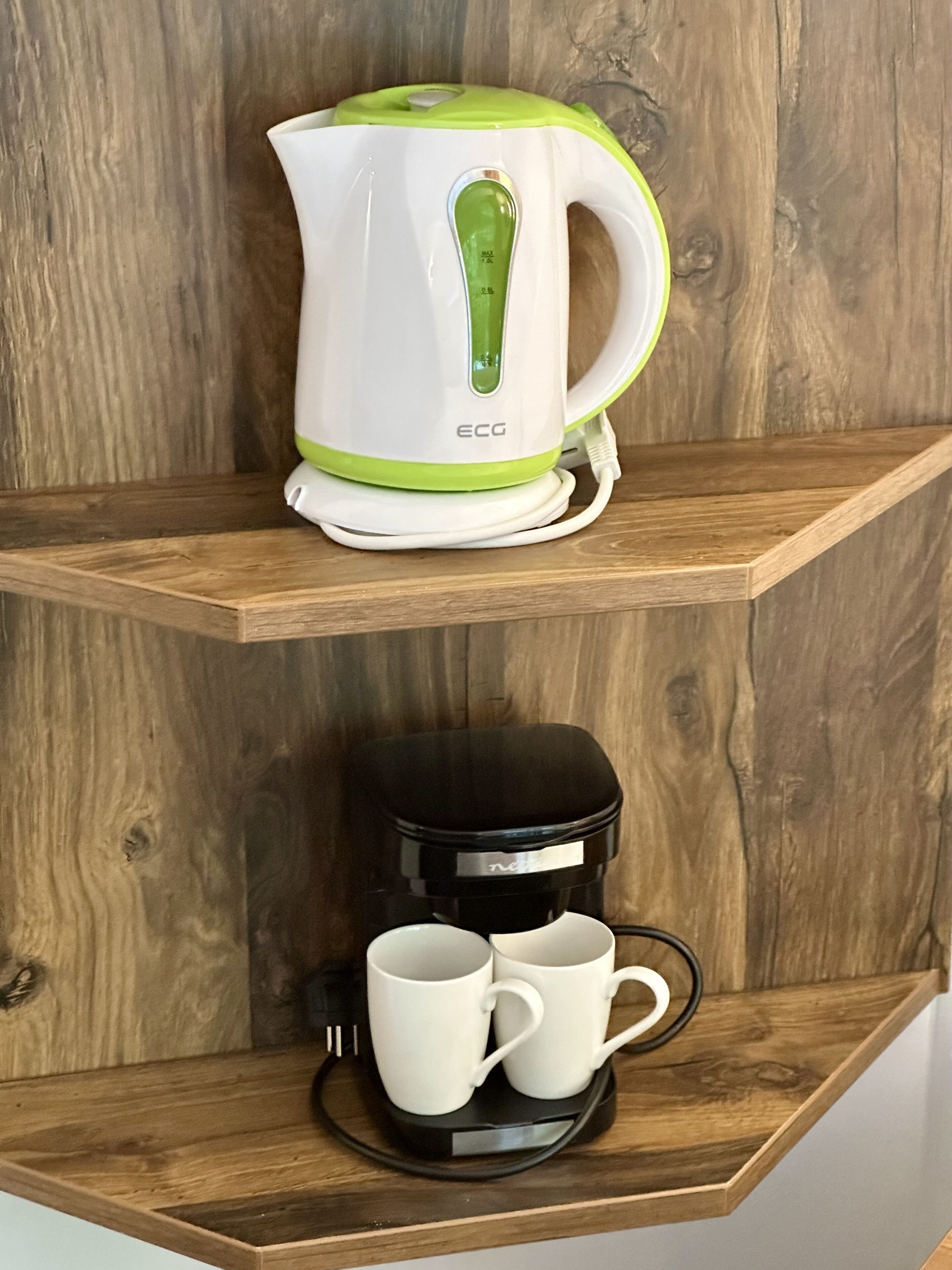 Un coin cuisine avec une bouilloire et une machine à café, le tout posé sur des étagères en bois.