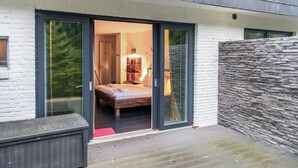 Een modern huis met een grote schuifdeur die leidt naar een slaapkamer met een bed en een nachtkastje.