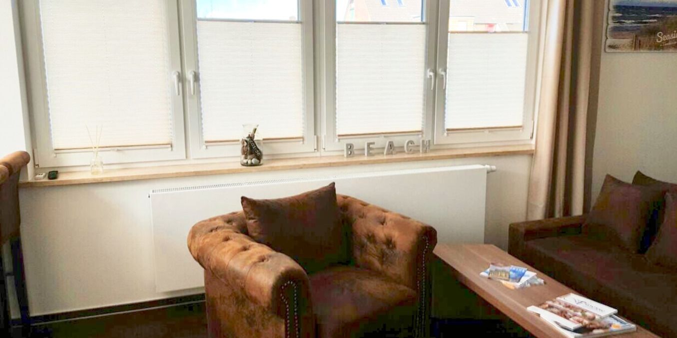 Ein Zimmer mit einem braunen Ledersessel, einem Holztisch mit Zeitschriften und einem Fenster mit Jalousien.