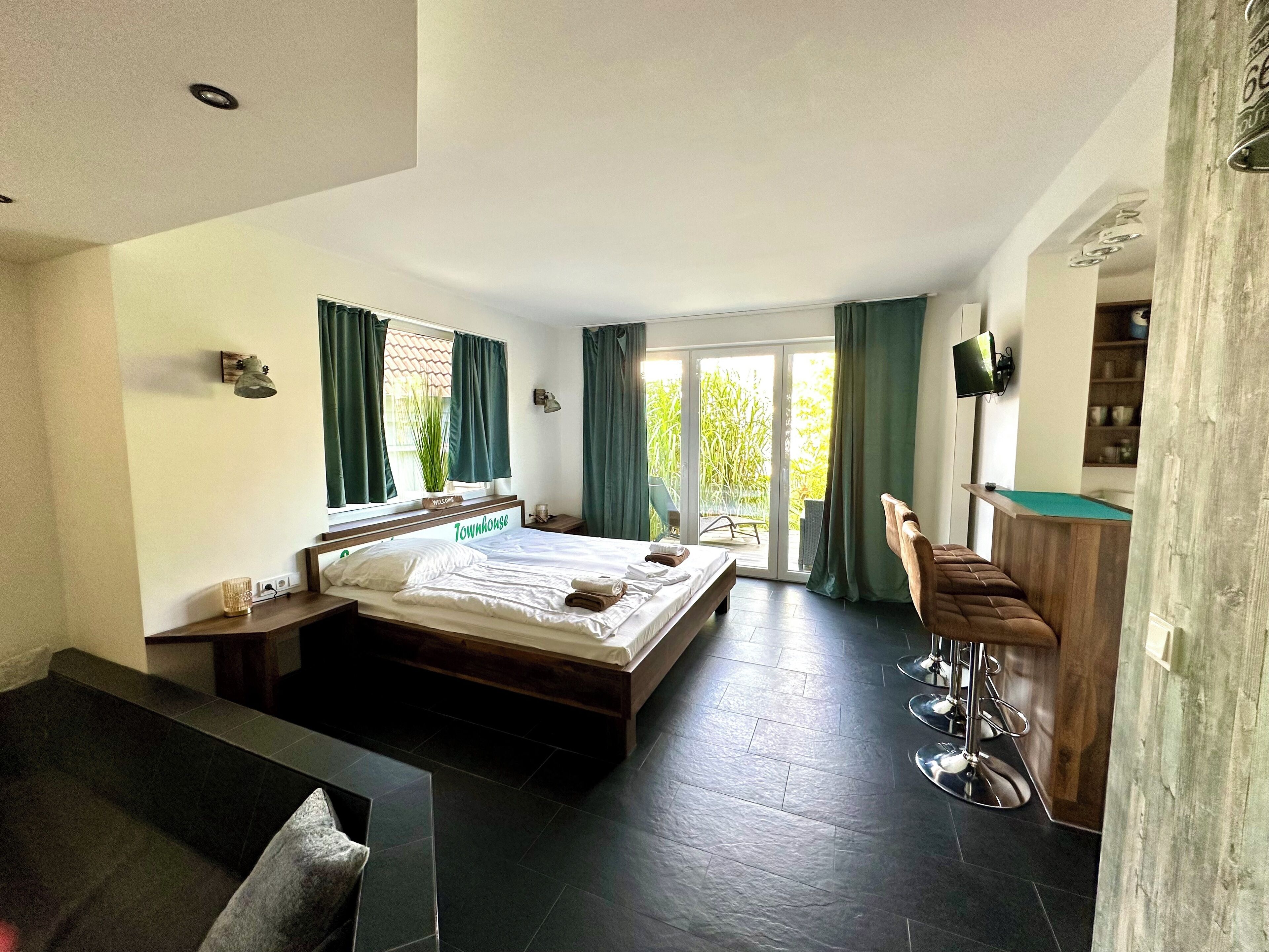 Une chambre d’hôtel moderne dotée d’un grand lit, d’un bureau en bois, d’un coin bar et d’une porte-fenêtre coulissante donnant sur l’extérieur.