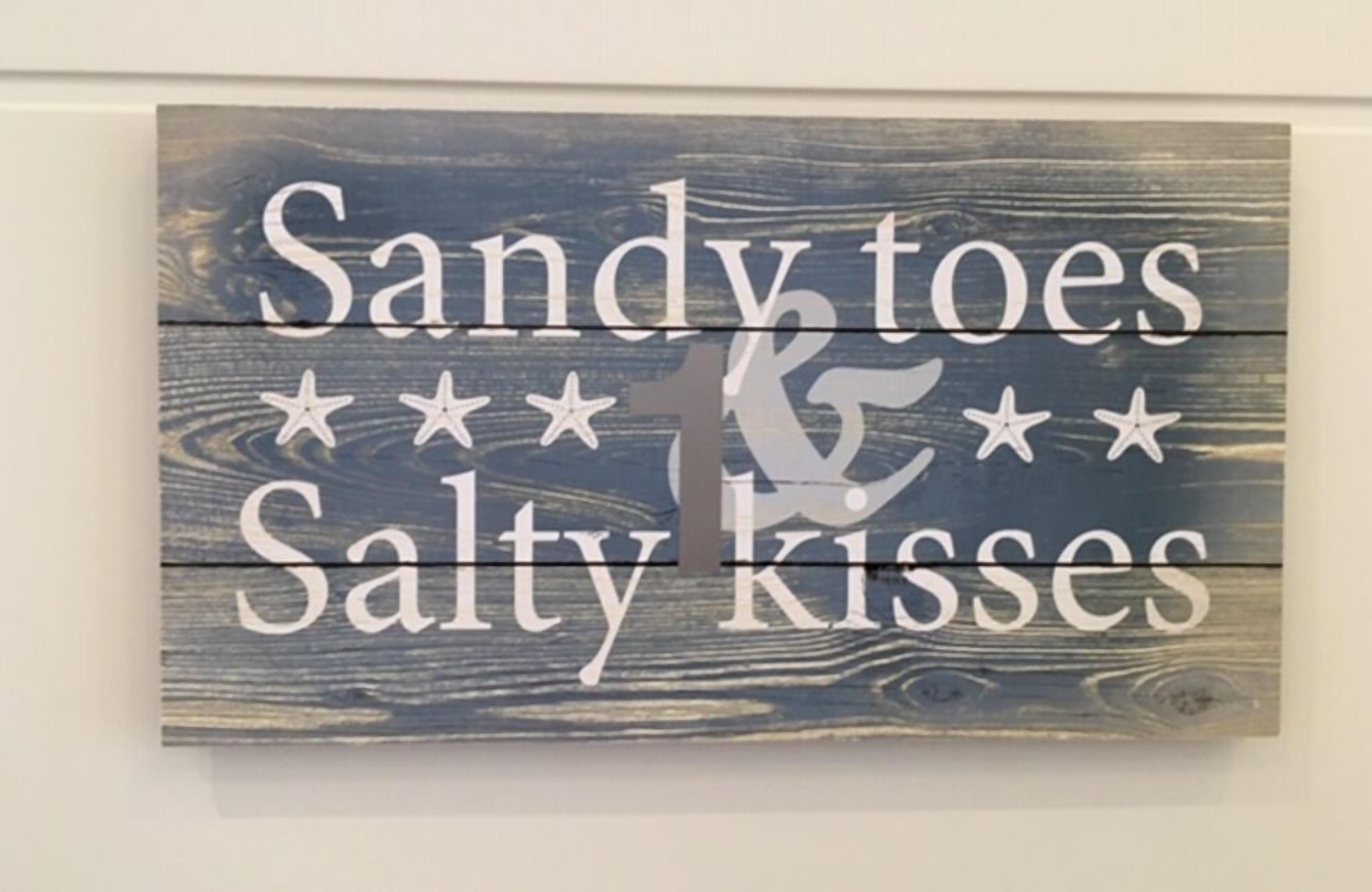 A wooden sign with the text "Sandy toes & Salty kisses" and decorative stars.