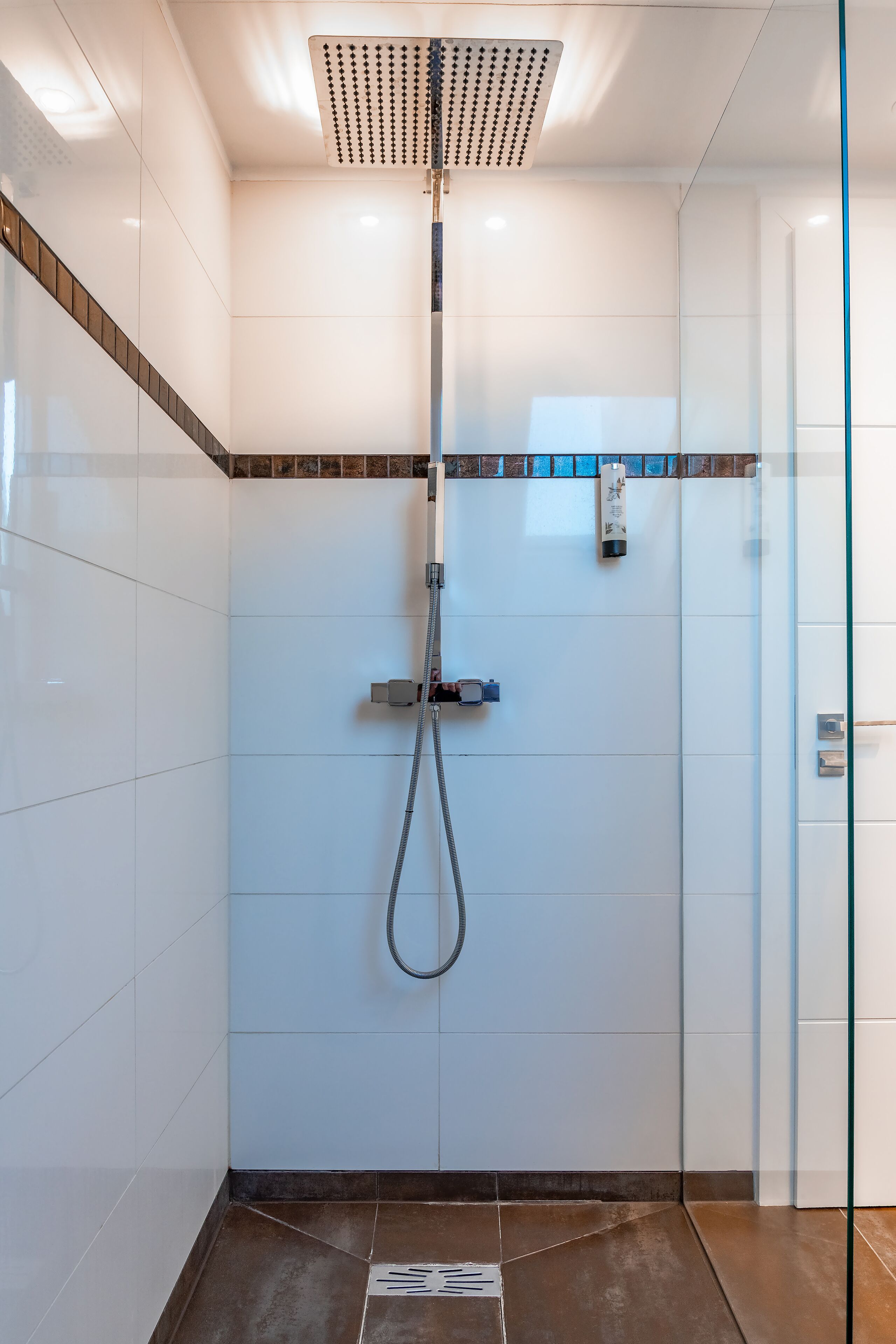 A modern shower with a rain showerhead, a handheld showerhead, and a handheld water pump.