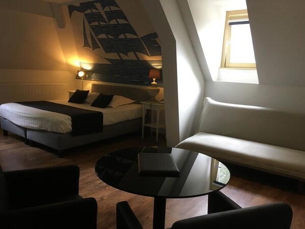 A modern bedroom with a bed, a sofa, a small table, and a staircase. - Hotel Fleur de Lys (Zedelgem)