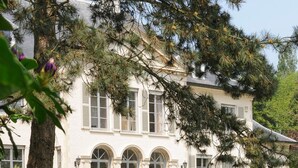 A white building with arched windows and a well-maintained lawn. - Hotel Fleur de Lys (Zedelgem)