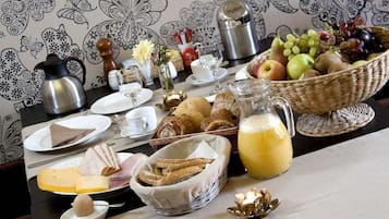 Una mesa de desayuno con diferentes alimentos, una cafetera y una cesta de frutas.