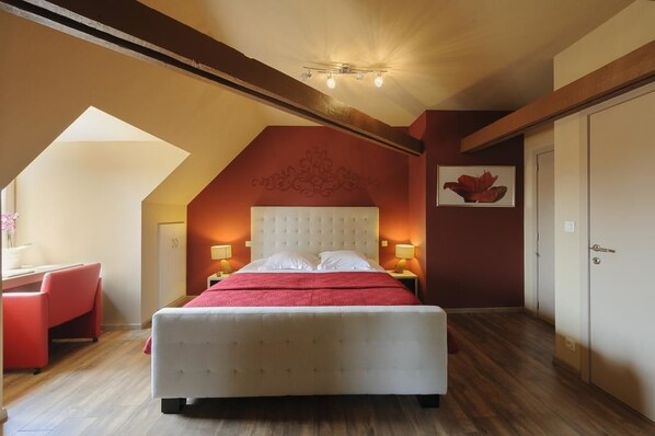 A bedroom with a large bed, a desk, and a chair. There is a ceiling light fixture and a door in the room.