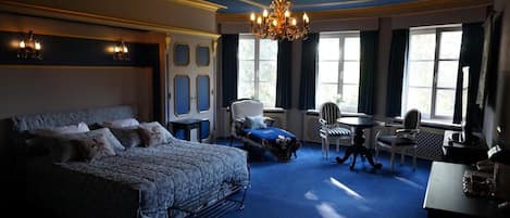 Un dormitorio espacioso con una cama grande, una zona de estar con una mesa y sillas, y una araña.