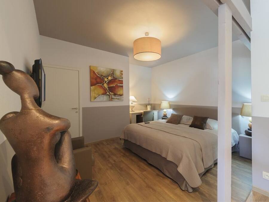 A bedroom with a bed, bedside lamps, a painting, and a sculpture.