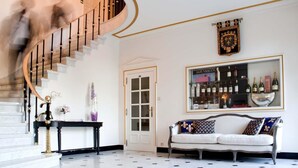 A grand staircase with a black and gold railing, a white door, and a bar area with bottles. - Hotel Fleur de Lys (Zedelgem)