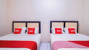 Una camera d'albergo con due letti, ciascuno con copripiumini e cuscini rossi e bianchi, e una coperta rossa sul pavimento.