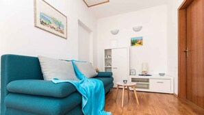 Ein blaustichiges Sofa mit blauer Decke, ein kleiner weißer Nachttisch und Holzboden.