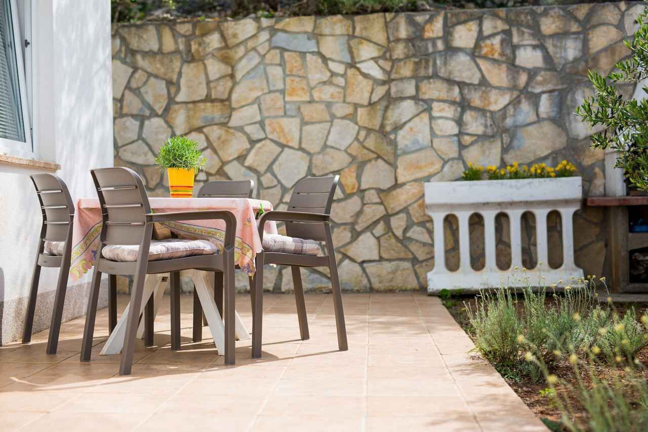An outdoor patio with a stone wall, a table with chairs, and a planter with plants.