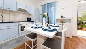 Eine moderne Küche mit hellblauen Schränken, einem weißen Esstisch mit blauen Platzsets und einem Fenster mit blauen Vorhängen.