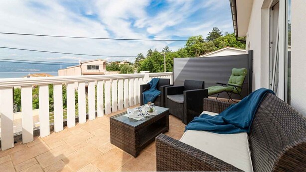 Ein Balkon mit Korbmöbeln, einem Glastisch und Blick aufs Meer.