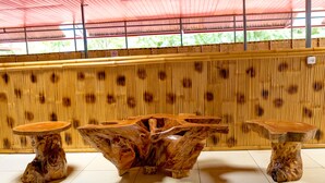 Une pièce avec une grande table en bois et deux petites tables d’appoint, un mur en bambou et un toit rouge.