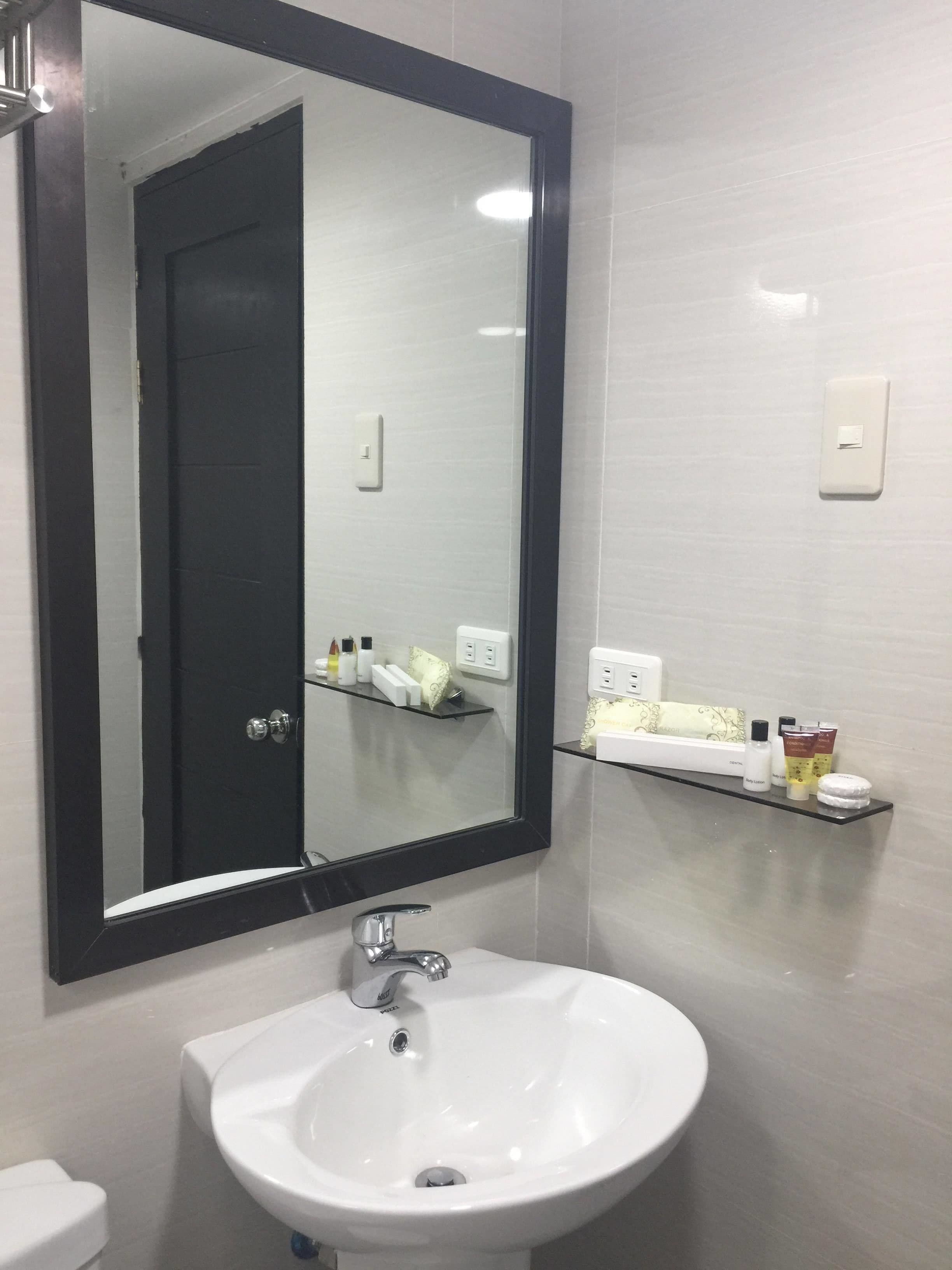 A bathroom with a white sink, a large mirror, and a shelf with toiletries.