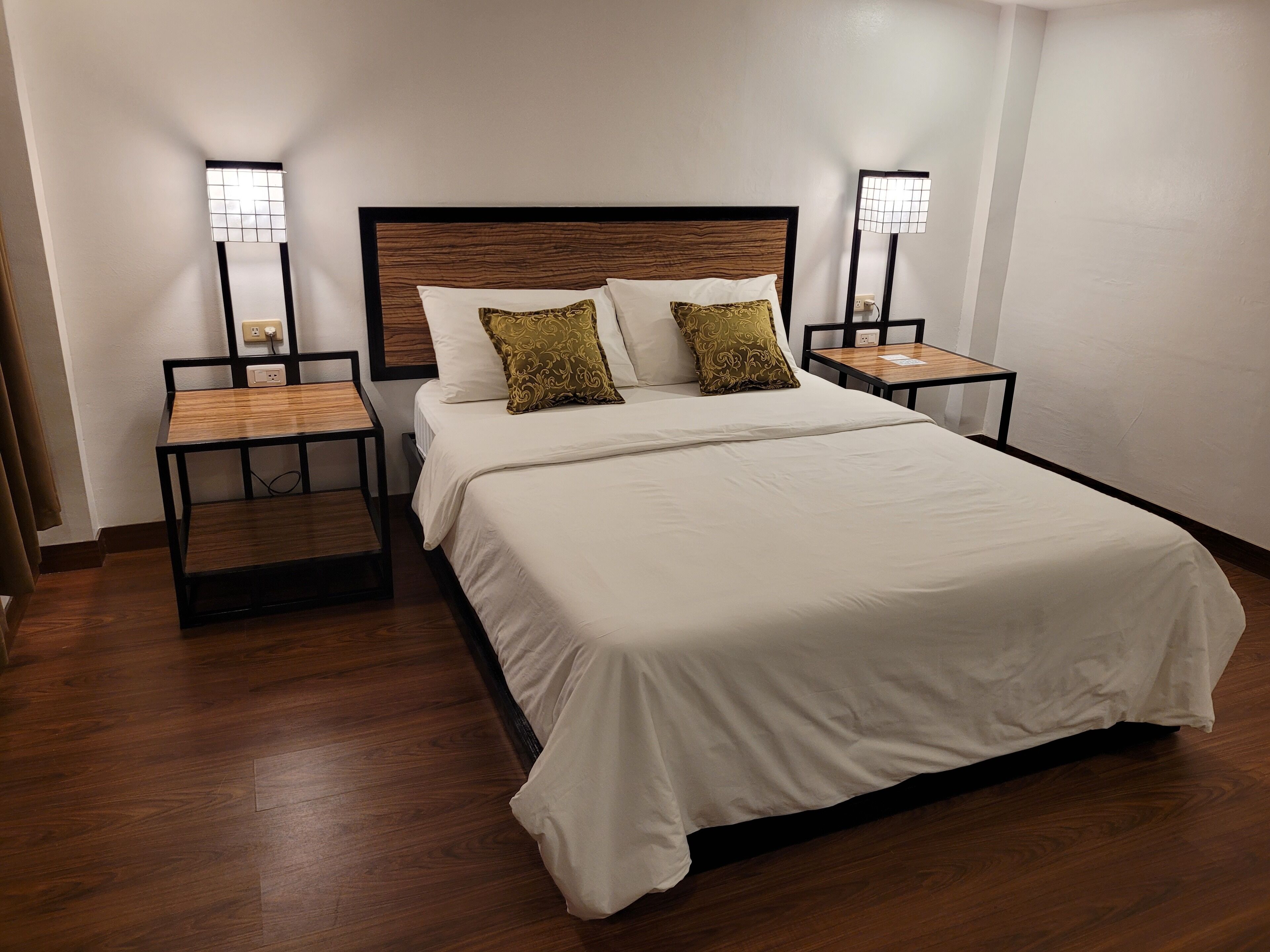 A neatly made bed with white linens and two decorative pillows, flanked by two bedside tables with lamps.