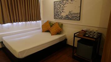 A small, neatly arranged room with a bed, a wall-mounted artwork, a small table with a basket, and a compact trash bin.