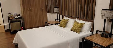 A hotel room with a large bed, wooden wardrobe, bedside tables, a desk, and a small refrigerator.