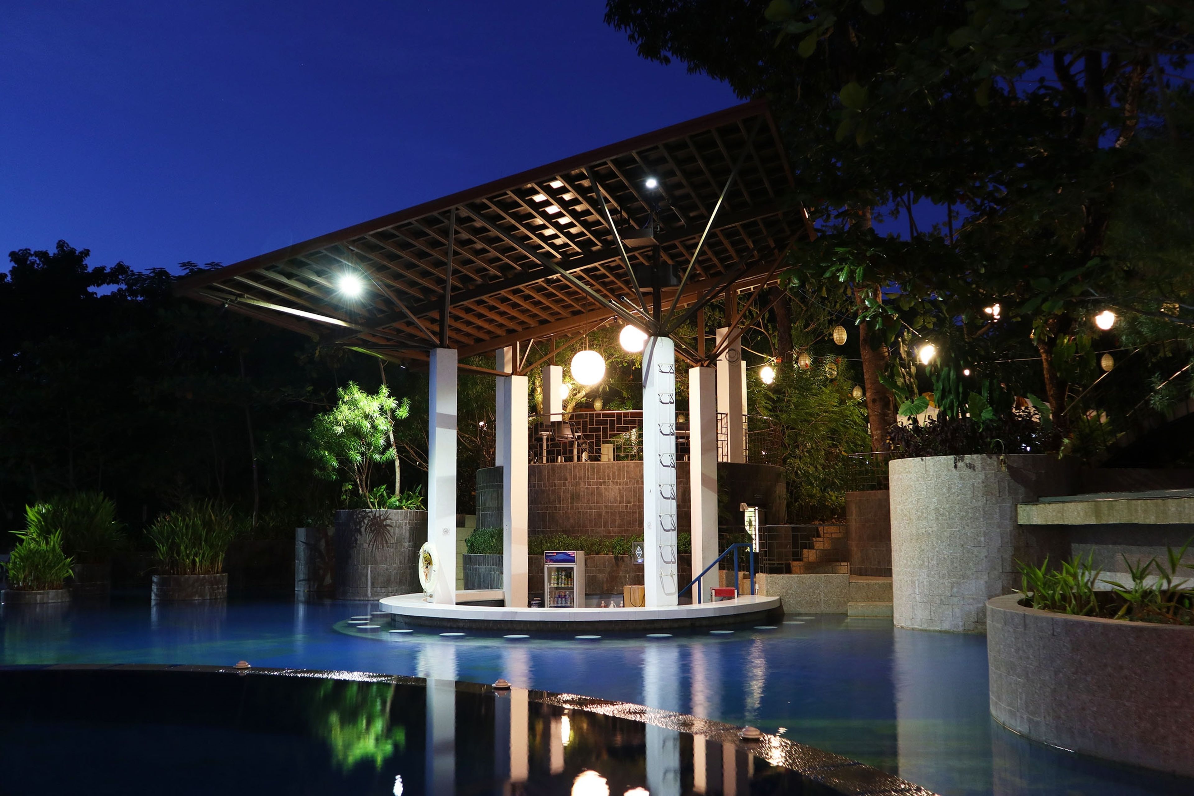 A pool area with a covered pavilion, stone columns, and string lights.