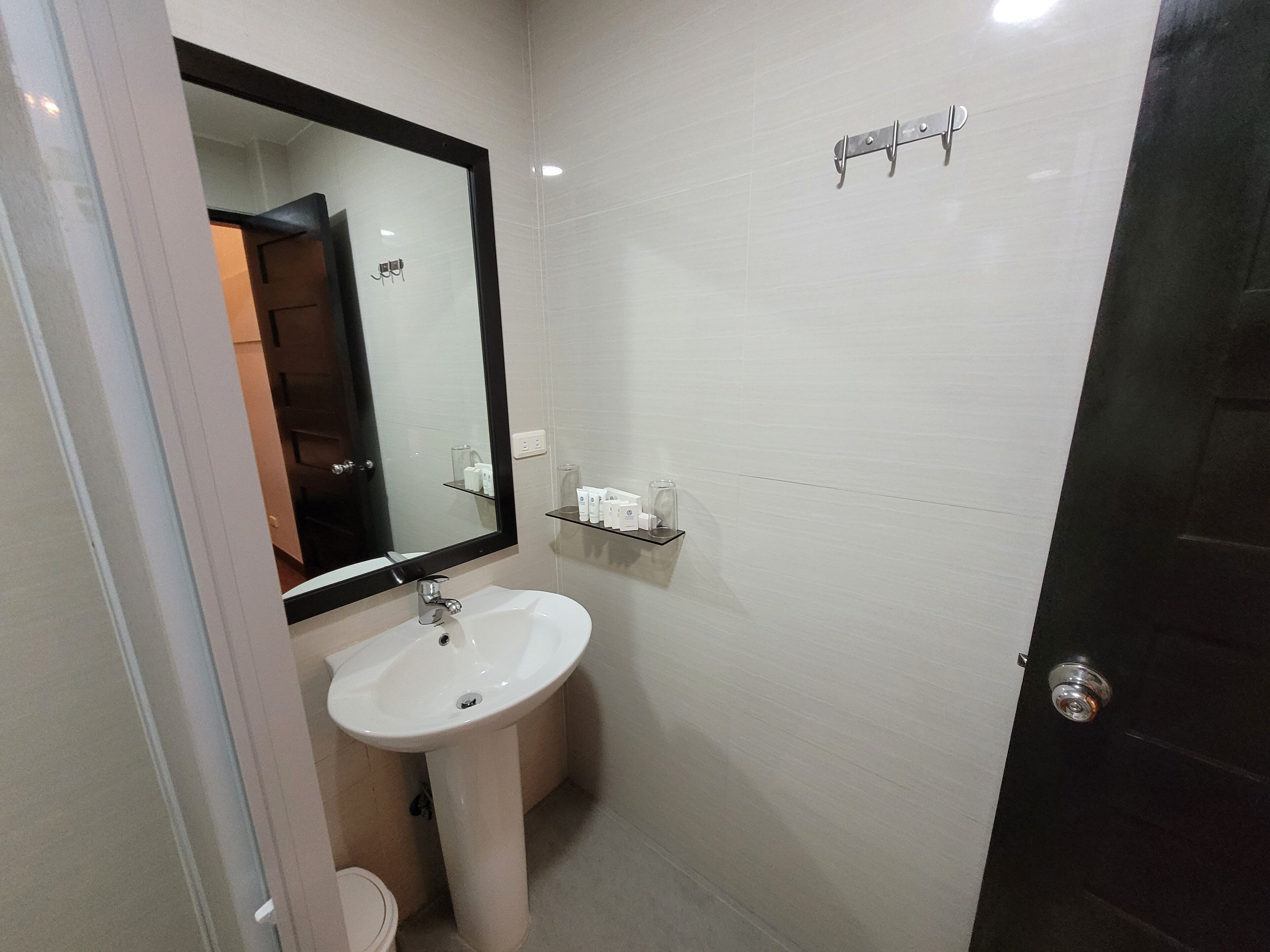 A bathroom with a white sink, a mirror, and a shelf with toiletries.