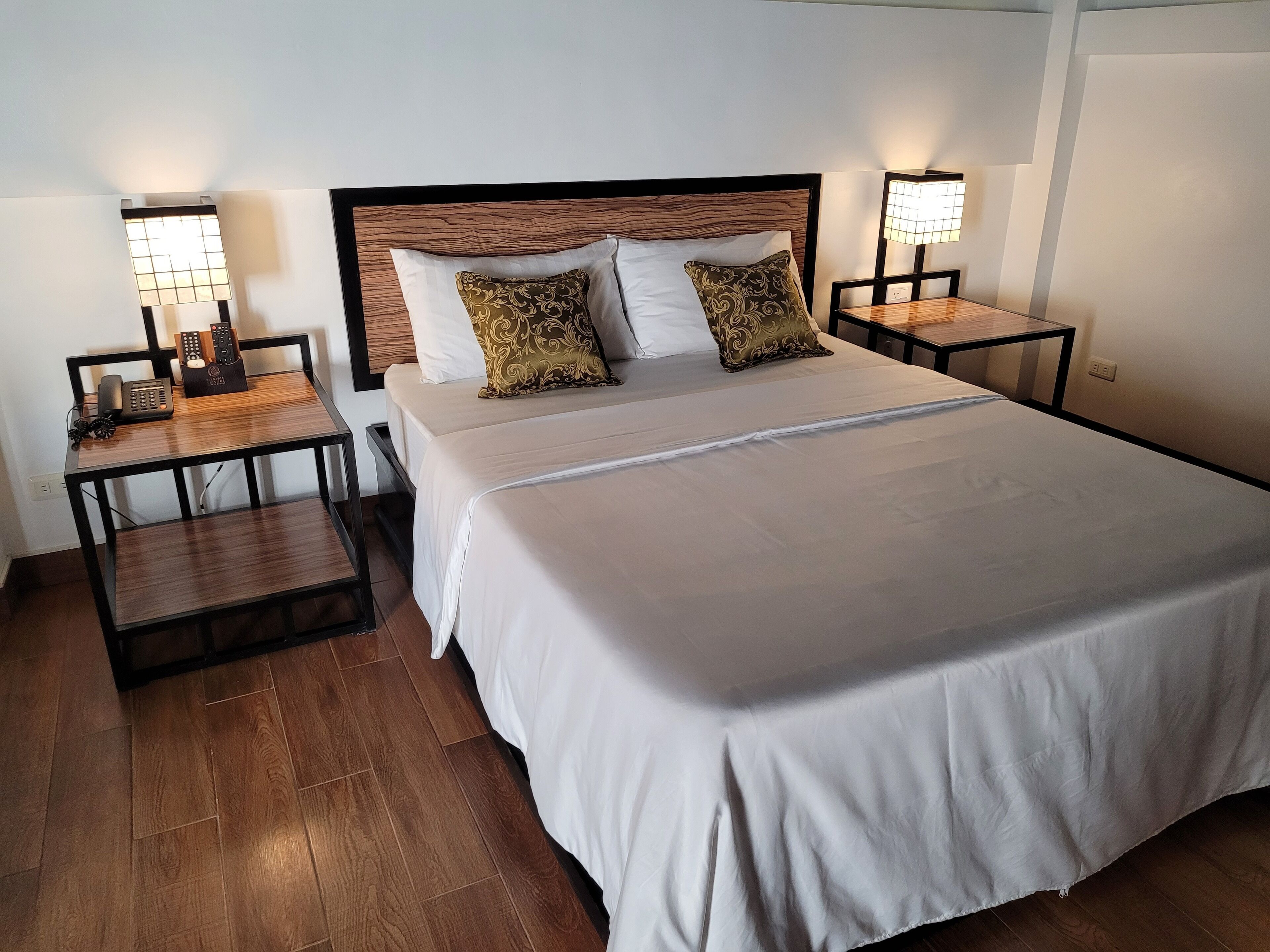 Ein ordentlich eingerichtetes Hotelzimmer mit einem großen Bett, zwei Nachttischen mit Lampen, einem Telefon und einem kleinen Tisch mit einer Lampe.