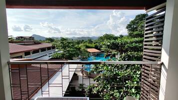 Relax on the balcony with a view of the pool surrounded by lush greenery and distant mountains.