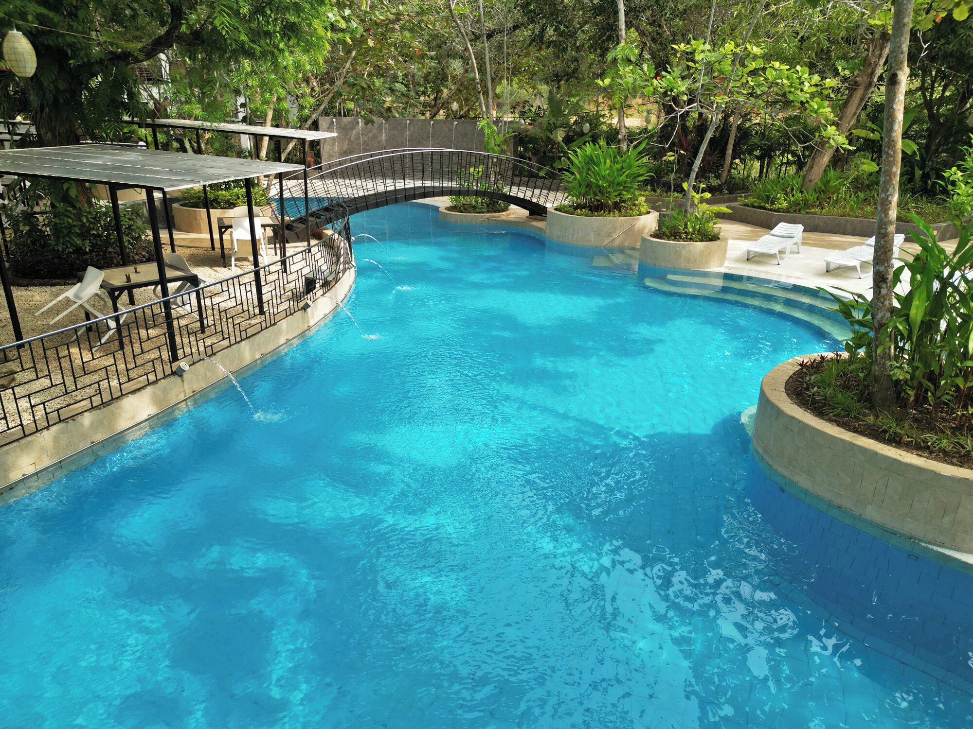 A swimming pool with a curved design, surrounded by lounge chairs and a covered seating area.