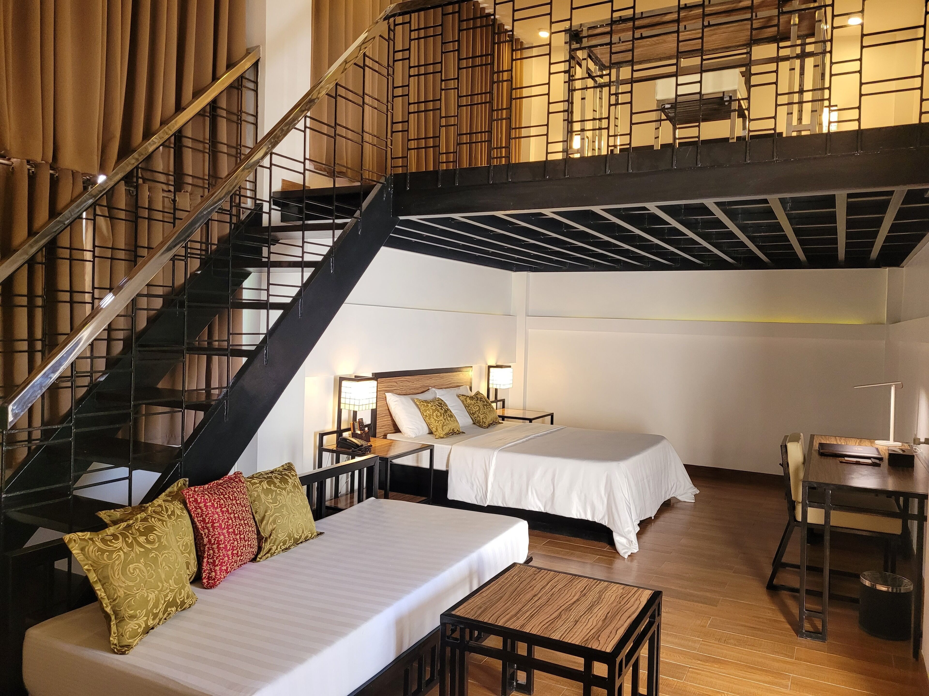A hotel room with a staircase, two beds, a small table, and a desk.