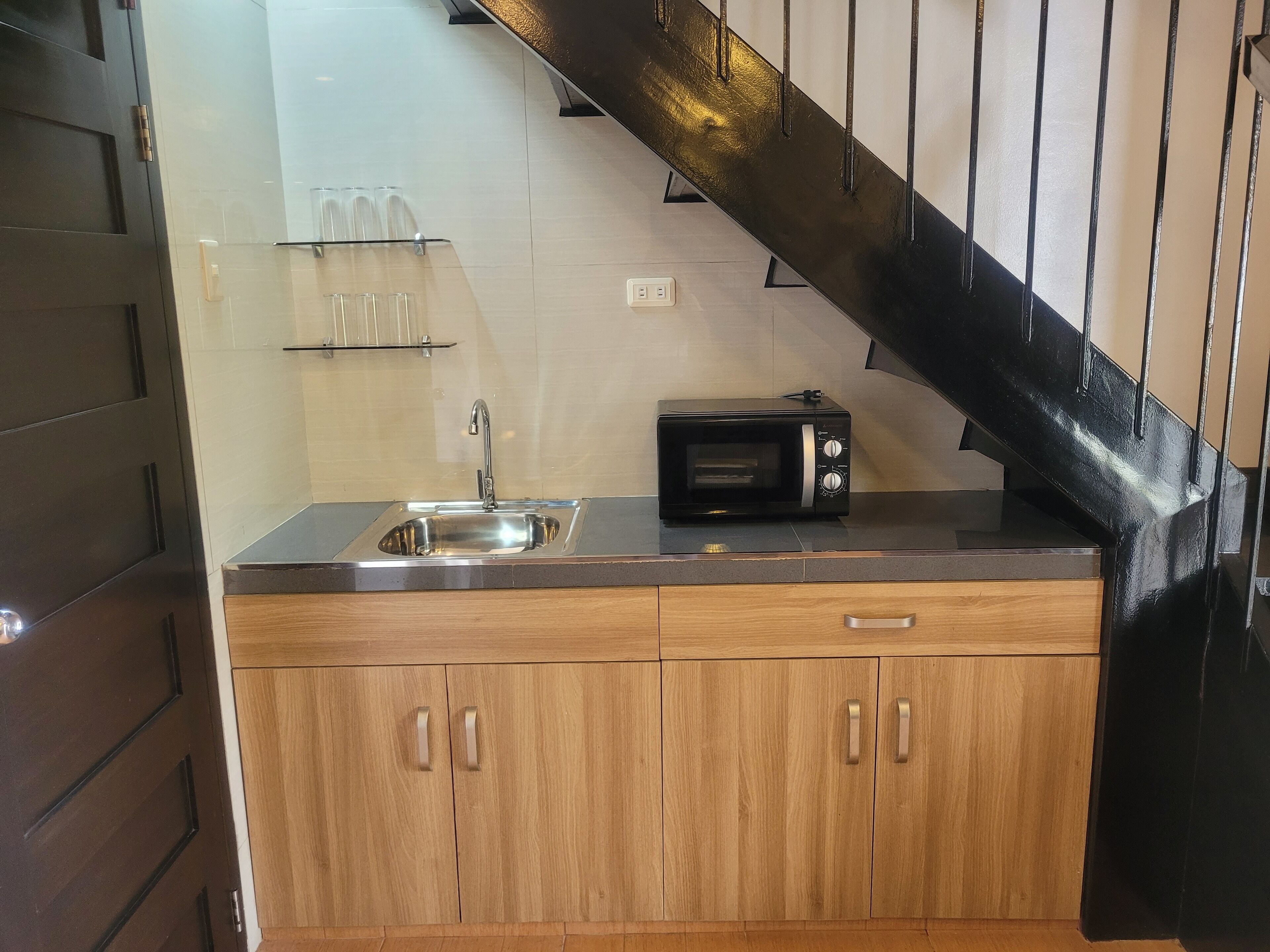 A compact kitchen with a stainless steel sink, a microwave, and wooden cabinets.