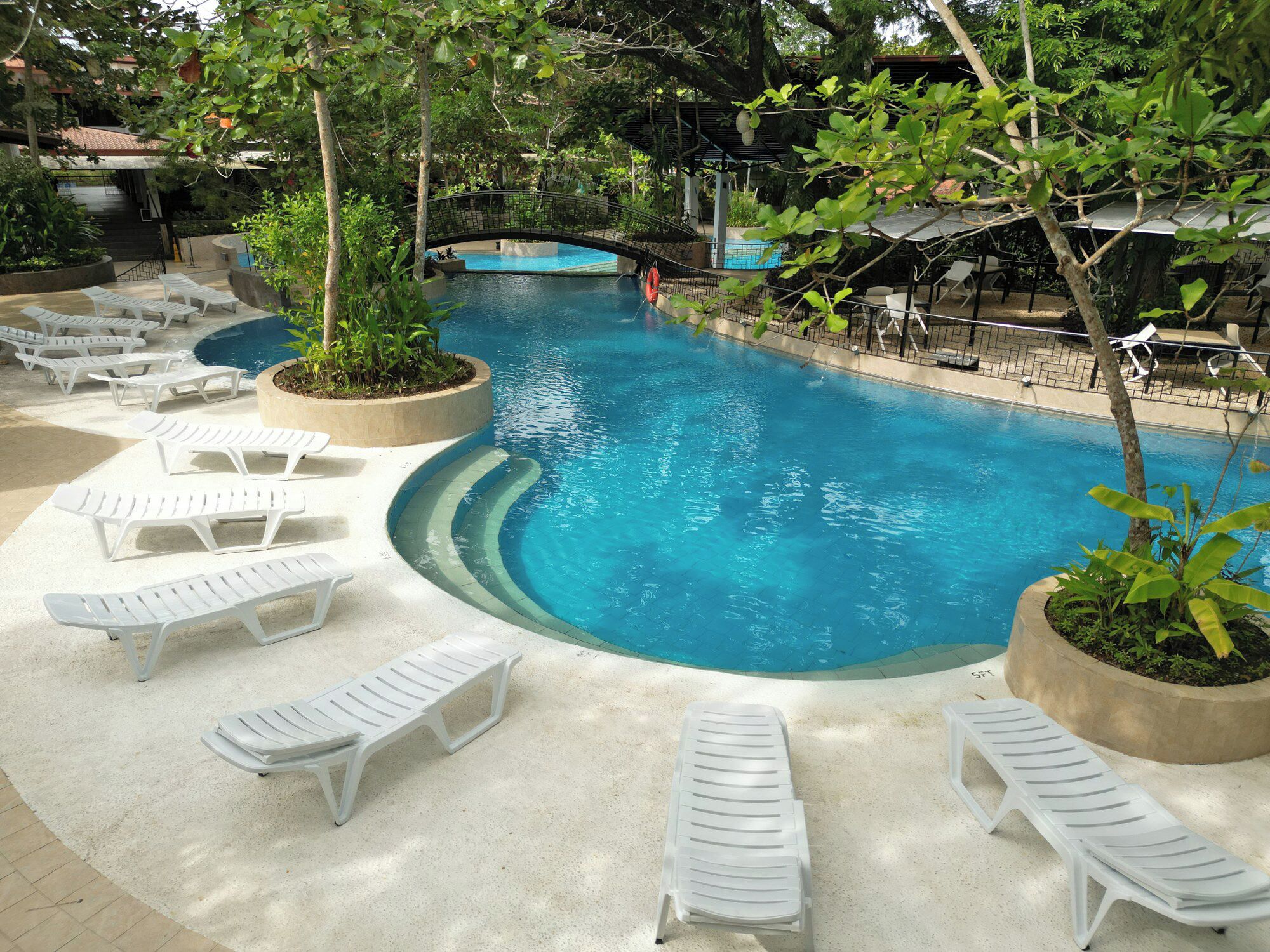 A pool area with white lounge chairs and a bridge over the water.