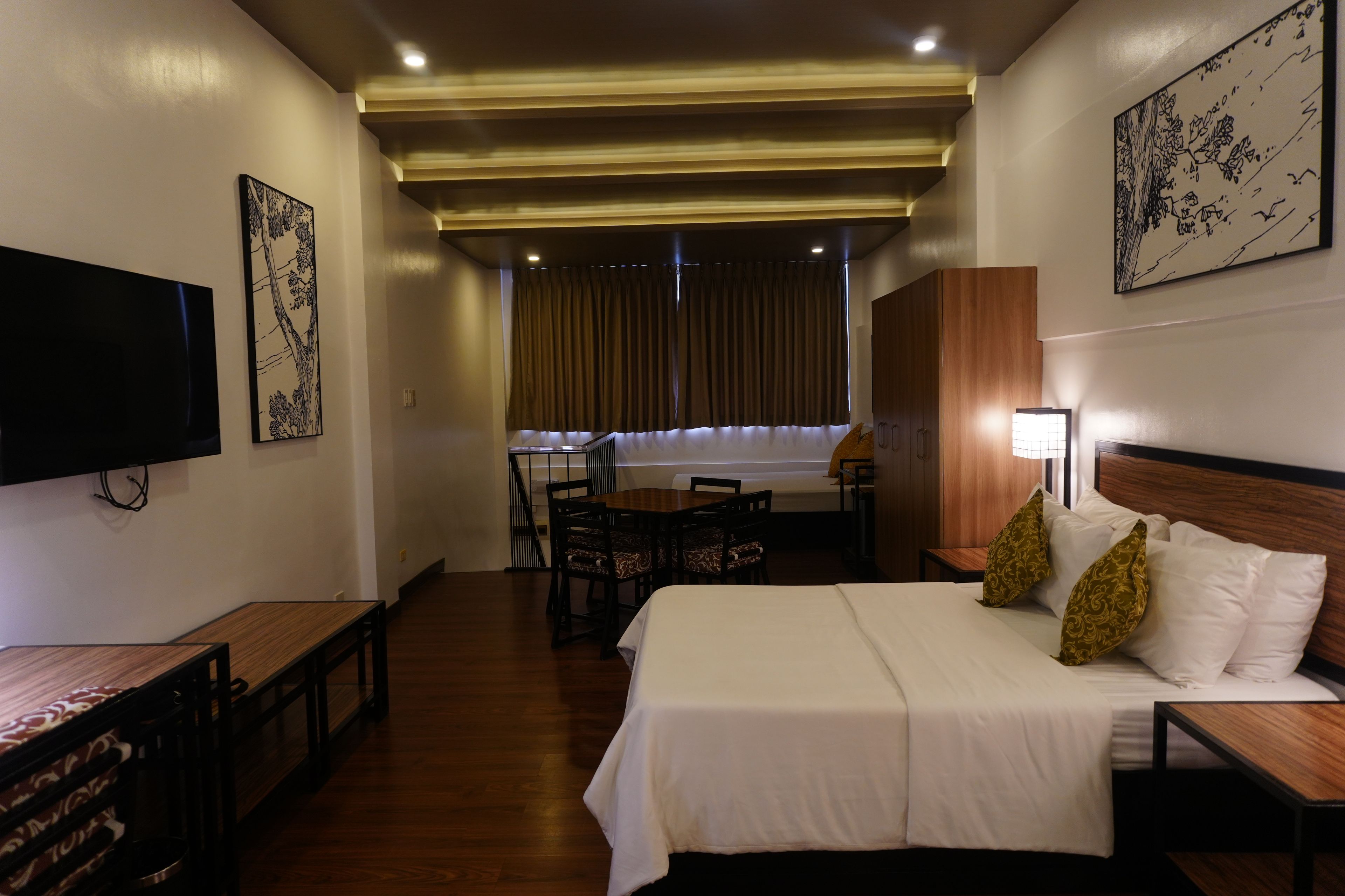 Una habitación de hotel con cama, escritorio, silla, televisión y obras de arte en las paredes.