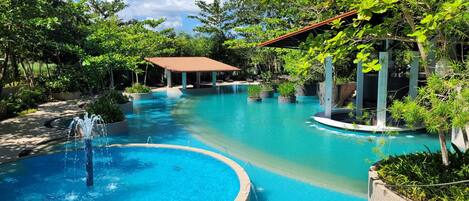 A swimming pool with a circular section, surrounded by lush greenery and a gazebo.
