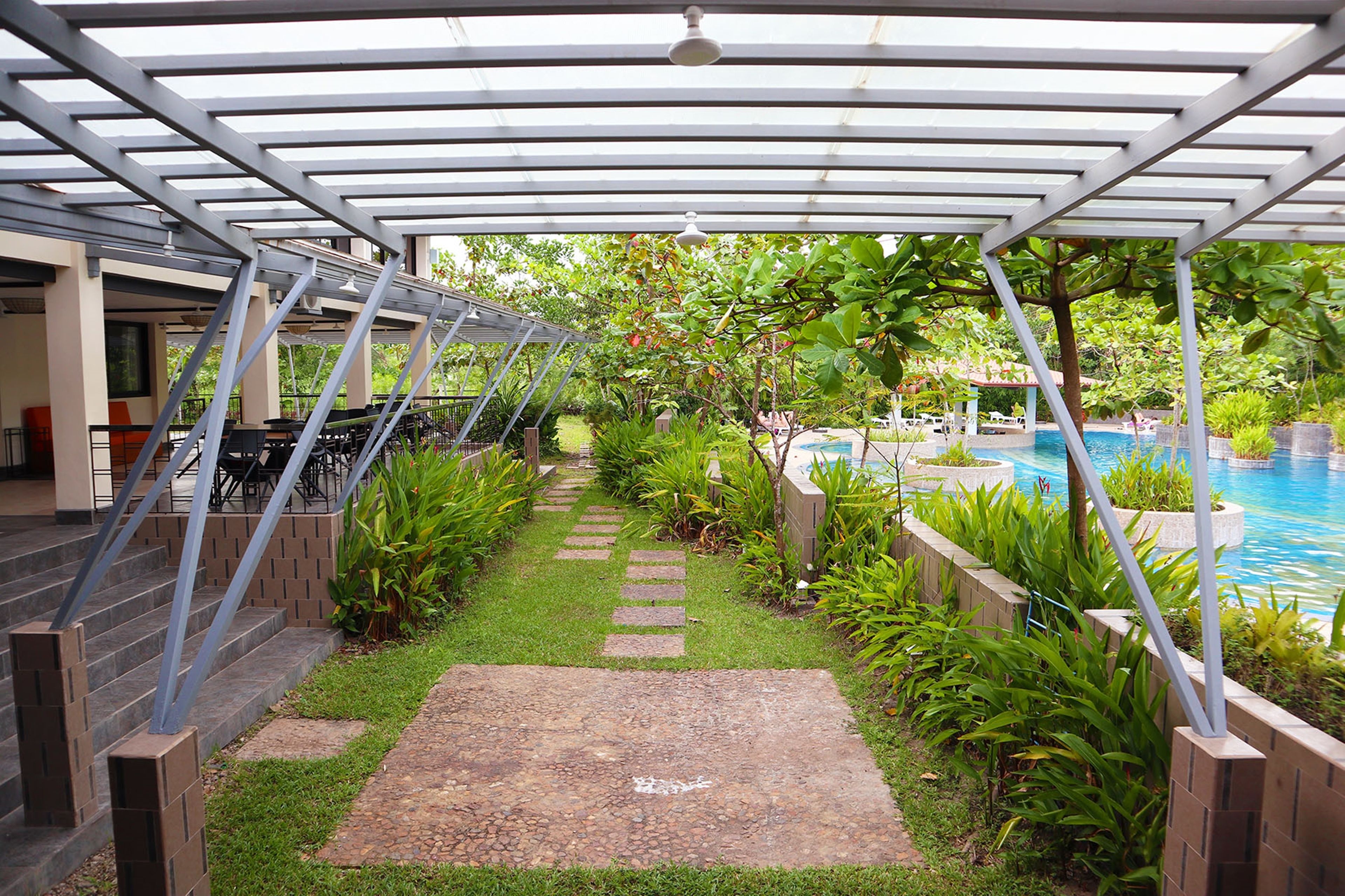 A covered outdoor area with a pool, stone pathway, and greenery.