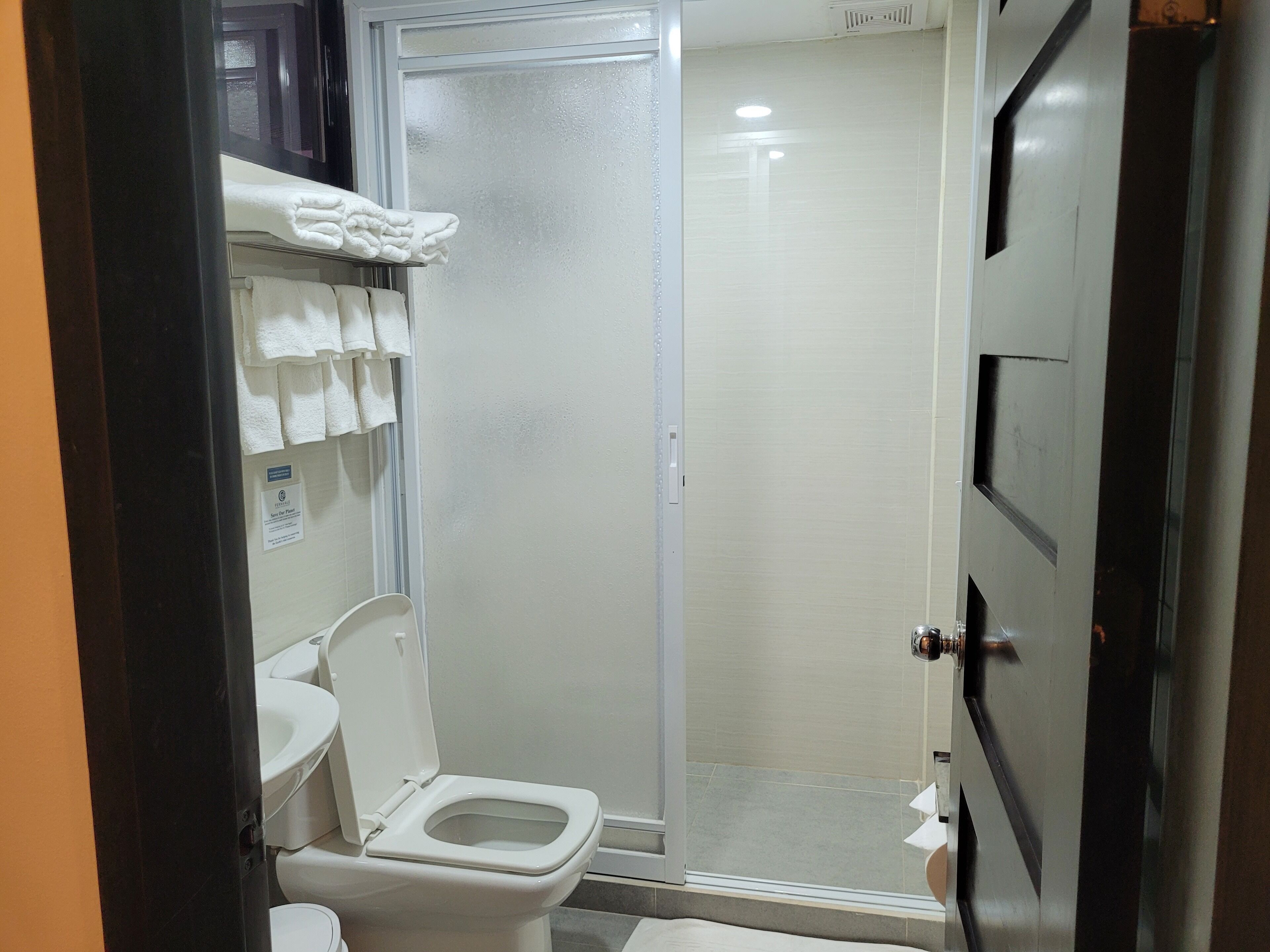 A bathroom with a toilet, a shower, and a towel rack with towels.