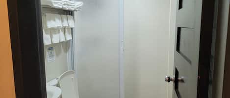 A bathroom with a toilet, a shower, and a towel rack with towels.