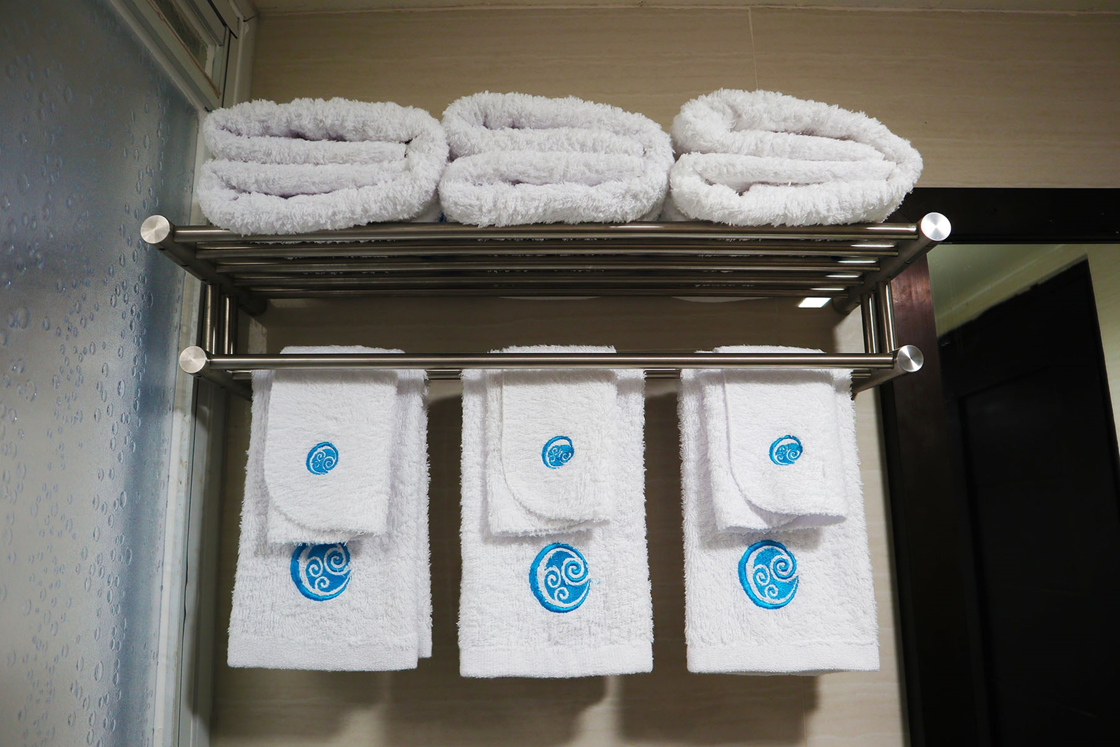 A metal towel rack with three folded towels and three towels with blue logos hanging below.