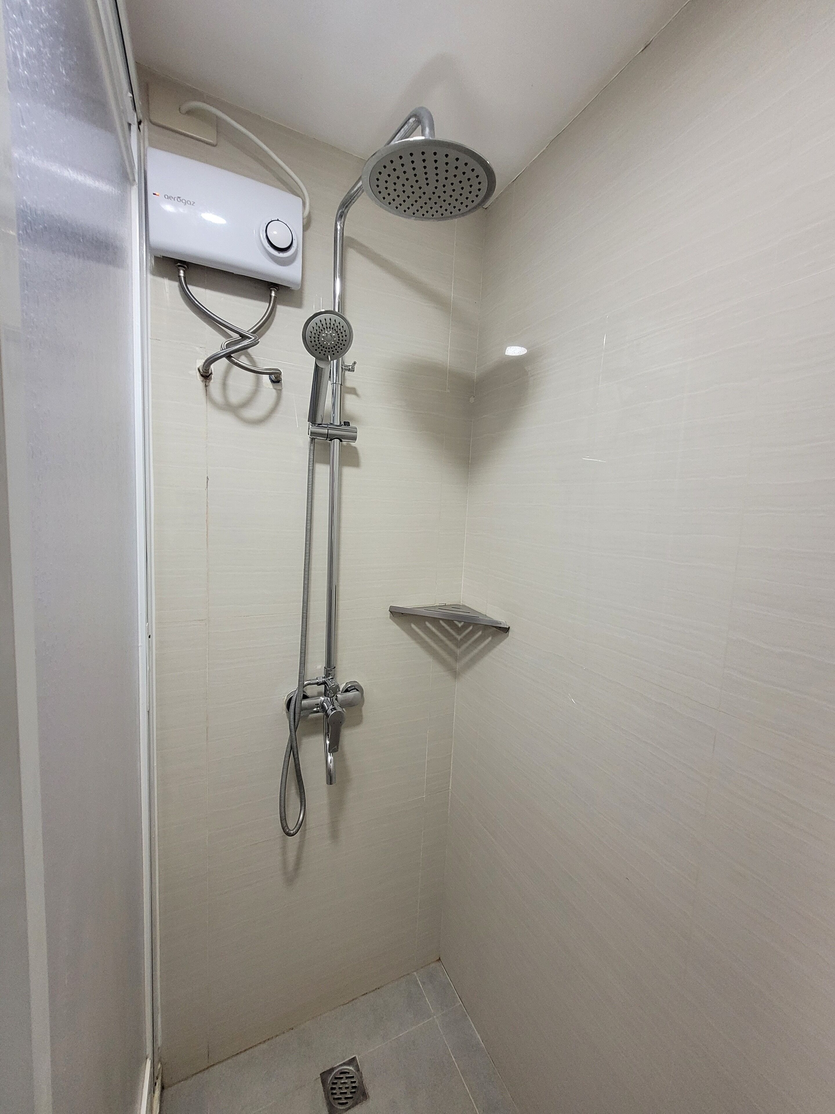A small, enclosed shower area with a handheld showerhead, a fixed showerhead, and a control panel.