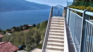 Una scala conduce a un balcone con ringhiera in metallo, affacciato su uno specchio d'acqua e montagne lontane.