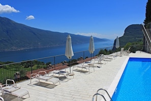 A poolside area with lounge chairs and umbrellas, overlooking a lake and mountains.